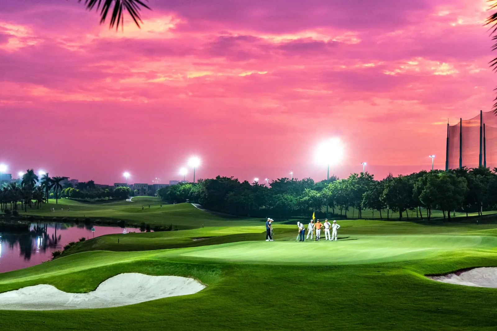 Golfers and caddies putting under floodlights at Long Bien Golf Course in Hanoi at dusk