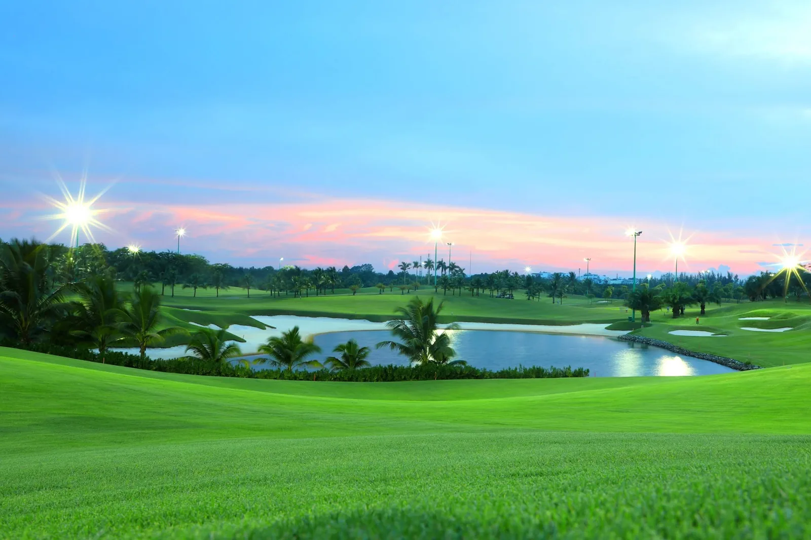 Floodlights switching on over the lake at Long Bien Golf Course at twilight